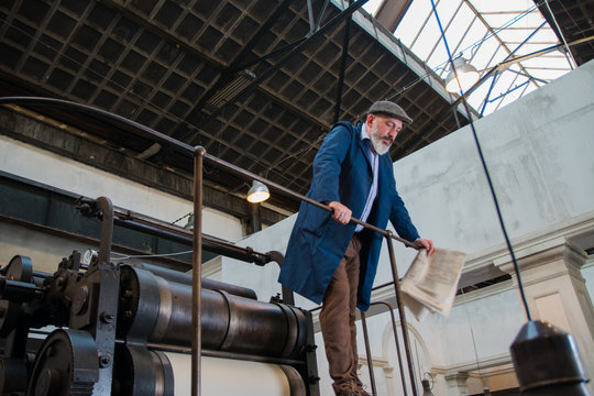 Worker standing on top platform of an old vintage press for newspaper printing