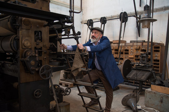 Blue collar worker climbing on a old printing machine