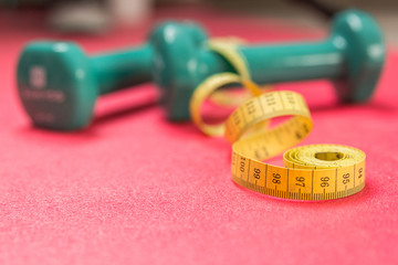 Wall Mural - Stock photo of two dumbbells and a measuring tape on an exercise mat