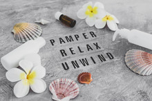 Natural Beauty Products, Lotions And Essential Oil Bottles Surrounded By Flowers And Shells With Pamper Relax Unwind Text