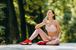 © speed300 - Brunette woman drinks a water  in earphones sitting in the park outdoors- Image