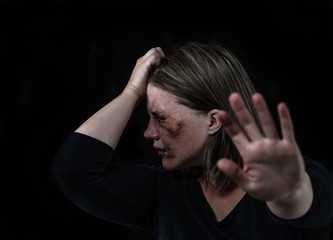 Wall Mural - Crying woman victim of domestic violence and abuse showing a stop sign and closes her mouth with her hand. Isolated on dark background