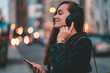 © Goffkein - Young happy stylish trendy casual hipster woman teenager listening to music on a black wireless headphone while walking around the city. Music lover enjoying music