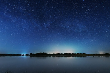 a magical starry night on the river bank with a large tree and a milky way in the sky and falling st