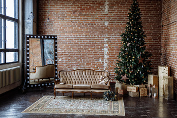 Wall Mural - Christmas interior. Living room in loft style with a brick wall and a sofa, with a large decorated Christmas tree, beautifully decorated for the holiday of Christmas or New year.