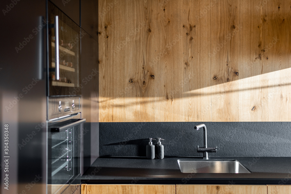 Modern minimalistic kitchen with black and wooden surfaces and household appliances on a sunlight - obrazy, fototapety, plakaty 