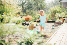 Little Blonde Girl Playing At Garden With Water In A Tin Basin. Kids Gardening. Summer Outdoor Water Fun. Childhood In The Country
