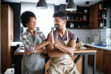 Canvas Print - Young happy couple in aprons giving high five in kitchen