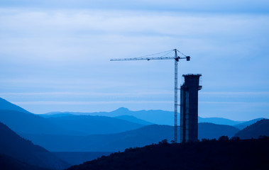 Large construction site including several cranes working on a building complex, with clear blue sky and the sun