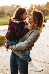 Beautiful mother holding on her arms her daughter looking at her against student in the park.