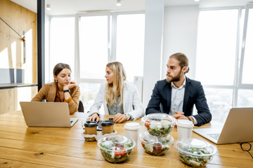 Poster - Office workers sitting in the office with business lunches on the foreground. Concept of healthy takeaway food on the work