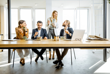 Group of a young office workers eating salads and drinking coffee at the modern office canteen. Concept of a healthy takeaway food on the work