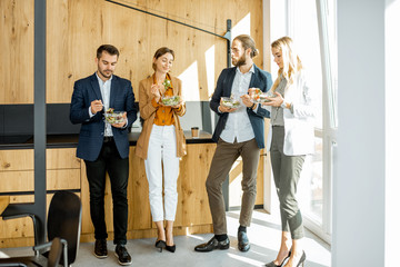 Group of a young office workers eating salads and drinking coffee at the modern office canteen. Concept of a healthy takeaway food on the work