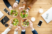 Office Workers During A Business Lunch With Healthy Salads And Coffee Cups, View From Above On The Wooden Table