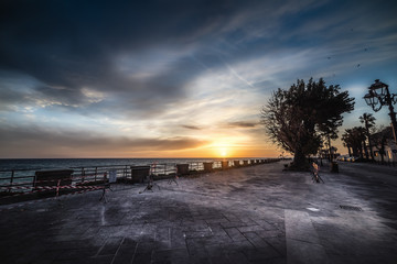 Wall Mural - Dark clouds over Alghero seafront at sunset