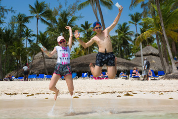 Poster - Happy teenagers keeping in hand blank pack of sth and jumping over water on tropical Bavaro beach in Punta Cana, Dominican Republic