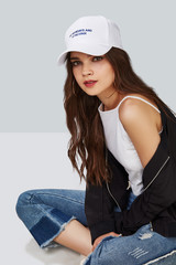 Wall Mural - Full length shot of a dark-haired girl, sitting on a floor and wearing white baseball cap with lettering 