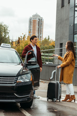 Woman with suitcase talking with taxi driver beside car