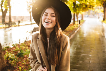 Poster - Portrait of joyful woman wearing coat and hat walking in autumn park