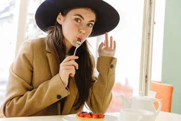 Sticker - Image of pleased young woman eating sweet cake at indoor cafe