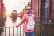Rear view of adult woman tourist with backpack enjoying sunset on the bridge in Speicherstadt historical warehouse district. Hamburg, Germany, Europe