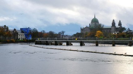 Wall Mural - Galway, Ireland. View of roman catholic cathedral of Galway, Ireland during the rainy day in autumn. River and cloudy sky, zoom out