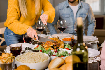 Wall Mural - Cropped image of pretty young mother hands cutting turkey for family on thanksgiving dinner. Festive table with tasty food