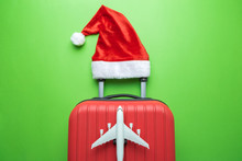 Suitcase With Santa Hat And Airplane Model On Green Background Minimal Creative Christmas Holiday Travel Concept.