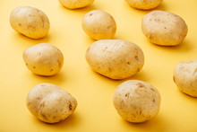 Pattern Of Raw Whole Fresh Potatoes On Yellow Background