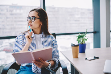 Wall Mural - pensive female author in eyewear looking away concentrated on idea for article sitting at desktop,sk
