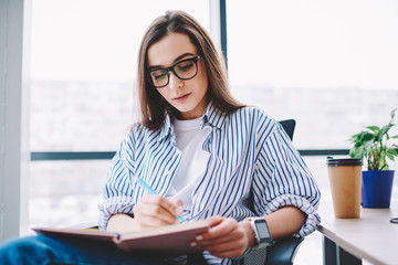 Wall Mural - serious female writer in spectacles concentrated on working process making notes of ideas at desktop