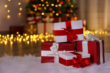 Wall Mural - Traditional christmas pine tree with holiday decorations on background and stack of presents on foreground. Bokeh lights glowing in the evening. Close up, copy space, background, interior.