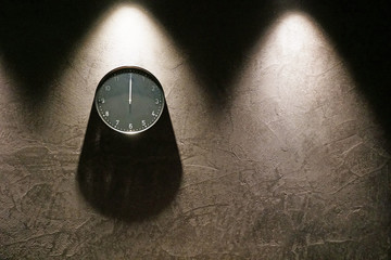 Black simple analog clock showing midnight hanging on the wall with shadows and copy space on the right