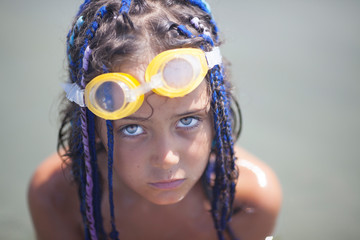 portrait of a little girl with dreadlocks and goggles for swimming on a background of water