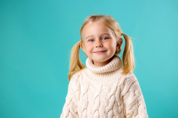 little blonde girl smiling in white knitted sweater on blue background