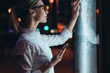 Wall Mural - interactive kiosk with public transport subway map.female standing at big display with smartphone in