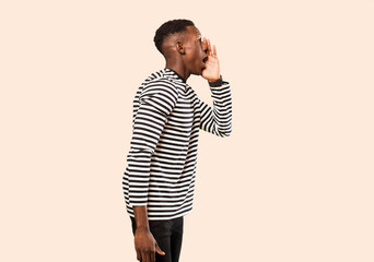 young african american black man profile view, looking happy and excited, shouting and calling to copy space on the side against beige wall