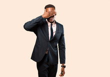 African American Businessman Covering Eyes With One Hand Feeling Scared Or Anxious, Wondering Or Blindly Waiting For A Surprise Against Beige Wall