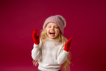 little blonde girl in a knitted hat and mittens smiles. winter clothes