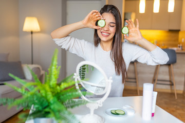 Woman holding cucumber slices on the face. Skin care, spa and beauty Treatments. Anti aging cosmetics. Smiling woman holding up two slices of cucumber next to her eyes, smiling happily