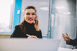 © BullRun - Half length portrait of prosperous female entrepreneur smiling at camera while talking on smartphone during phone call working in office interior.Cheerful manager have mobile conversation on cellular
