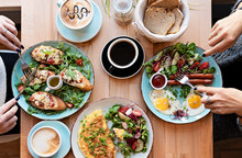 Different Colorful Meals For Breakfast Or Lunch Time On A Plate With Cutlery On Woman's Hands. Fried Eggs, Omelette, Bruschetta And Sausage On A Wooden Teble In Restaurant. Flat Lay Top View.