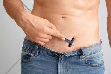 Wall Mural - Handsome young man shaving his body on light background, closeup