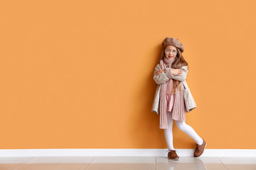 fashionable little girl in autumn clothes near color wall