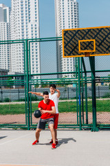 Wall Mural - Basketball players playing ball(pushing, dribbling) on an urban basketball ground while the white skyscrapers nearly touch the blue sky.