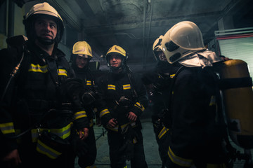 Team of firefighters standing inside ( indoors ) a buliding next to a fire engine.