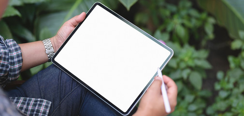 Wall Mural - Cropped shot of businessman working on his project with blank screen tablet with garden background