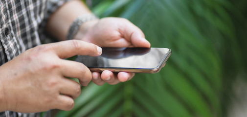 Cropped shot of professional businessman using smartphone with garden background