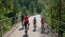 Family Of Caucasian Parents And Children In Bicycles Crossing A Bridge Together In Slovenia, Drone Flies Up At The End To Let Them Pass