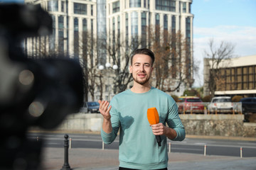 Wall Mural - Young male journalist with microphone working on city street